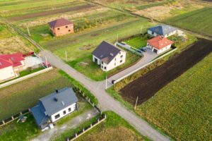 Obraz lotniczy przedstawiający proces budowy energooszczędnego domu stalowego na tle wiejskiego krajobrazu.